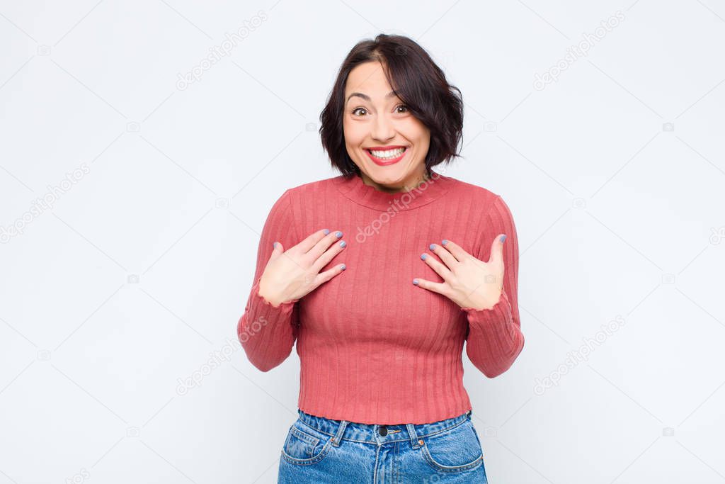 young pretty woman looking happy, surprised, proud and excited, pointing to self against white wall