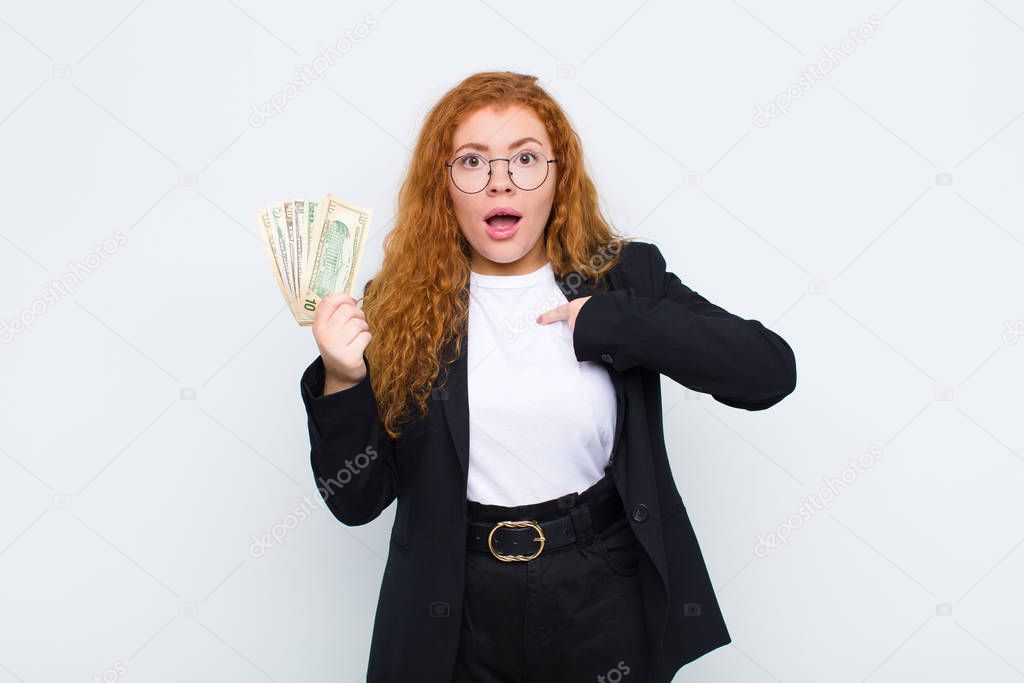 red head young woman feeling happy, surprised and proud, pointing to self with an excited, amazed look against white wall