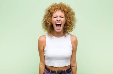 Genç afro kadın saldırganca bağırıyor, çok kızgın, sinirli, öfkeli ya da sinirli görünüyor, yeşil duvara karşı hayır diye bağırıyor.