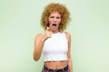 Kızgın ve agresif bir ifadeyle kameraya bakan genç bir afro kadın yeşil duvara karşı öfkeli, çılgın bir patron gibi görünüyor.