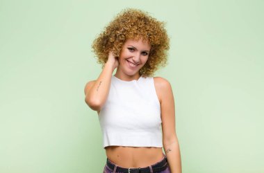 Genç afro kadın, yeşil duvarın karşısında neşeli ve kendinden emin bir şekilde gülüyor.