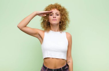 Genç afro kadın, yeşil duvara saygı göstererek, onur ve vatanseverlik eylemiyle kamerayı selamlıyor.