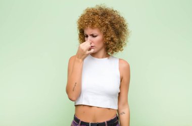 Genç afro kadın iğreniyor, yeşil duvardaki pis ve nahoş kokuyu koklamamak için burnunu tutuyor.