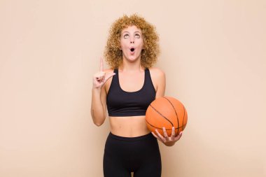 Genç afro kadın şaşkın, şaşkın ve ağzı açık görünüyor, uzay sporu konseptini kopyalamak için iki elini havaya kaldırıyor.