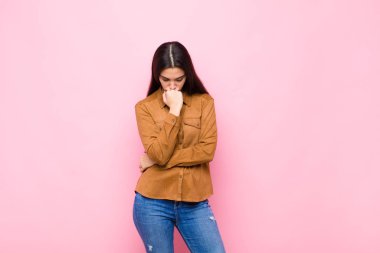 Genç ve güzel bir kadın ciddi, düşünceli ve endişeli, elleri pembe duvara yaslanmış bir şekilde yan bakıyor.