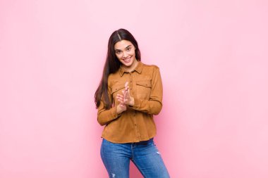 Genç, güzel bir kadın kendini mutlu ve başarılı hissediyor. Gülümsüyor ve alkışlıyor. Pembe duvara karşı alkışlarla tebrik ediyor.