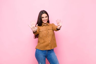 Genç, güzel bir kadın gülümsüyor ve arkadaş canlısı görünüyor. 9 ya da 9 numarayı gösteriyor. Elleri önde, pembe duvara doğru sayıyor.