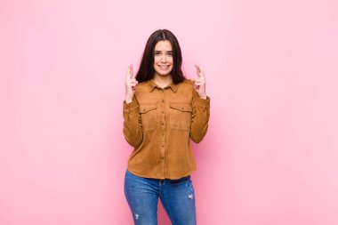 Genç ve güzel bir kadın endişeyle pembe duvara karşı endişeli bir bakışla iyi şanslar diliyor.