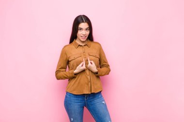 Genç ve güzel bir kadın, şaşkın ve tuhaf bakışlarıyla kendini işaret ediyor. Pembe duvara karşı seçildiği için şaşırmış ve şaşırmış.