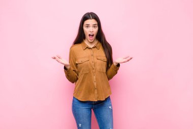 Genç ve güzel bir kadın son derece şaşkın, şaşırmış, endişeli ve paniklemiş hissediyor. Pembe duvara karşı stresli ve dehşetli bir bakışla bakıyor.