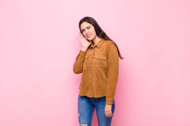 Genç ve güzel bir kadın ciddi ve meraklı görünüyor, dinliyor, gizli bir konuşma ya da dedikodu duymaya çalışıyor, pembe duvara kulak misafiri oluyor.