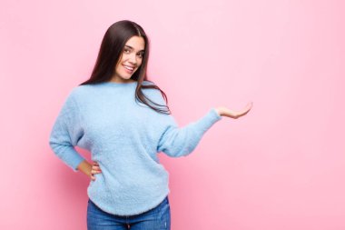 Genç, güzel bir kadın gülümsüyor, kendine güveniyor, başarılı ve mutlu, fotokopi odasında pembe duvara karşı fikir veya konsept gösteriyor.