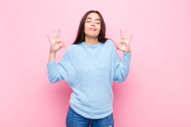 Genç ve güzel bir kadın konsantre olmuş ve meditasyon yapıyor. Tatmin olmuş ve rahatlamış hissediyor. Pembe duvara karşı bir seçim yapıyor.