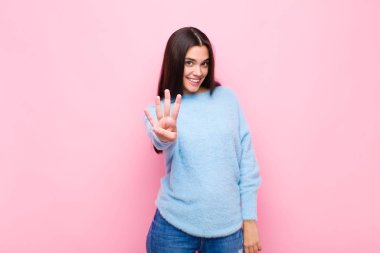 Genç ve güzel bir bayan gülümsüyor ve arkadaş canlısı görünüyor, dört ya da dört numarayı gösteriyor, elini ileri uzatmış, pembe duvara doğru sayıyor.