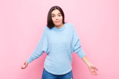 Genç, güzel bir kadın kendini cahil ve şaşkın hissediyor. Hiçbir fikri yok. Pembe duvara karşı aptal ya da aptal bir bakışla kafası karışmış.