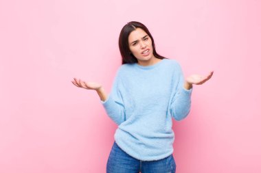 Genç, güzel bir kadın kendini cahil ve şaşkın hissediyor. Hangi seçeneği seçeceğinden emin değil. Pembe duvara karşı merak içinde.