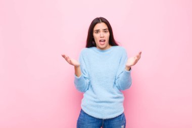 Genç ve güzel bir kadın son derece şaşkın, şaşırmış, endişeli ve paniklemiş hissediyor. Pembe duvara karşı stresli ve dehşetli bir bakışla bakıyor.