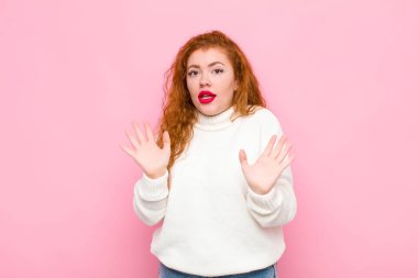 Genç kızıl saçlı kadın gergin, endişeli ve endişeli görünüyor. Benim hatam olmadığını söylüyor. Yoksa pembe duvara karşı yapmazdım. 