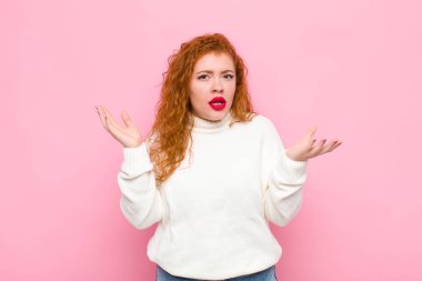 Genç kızıl saçlı kadın şaşkın ve şaşkın bakıyor, pembe duvara karşı inanılmaz bir şey fark ettiğinde çenesi şaşkın şaşkın