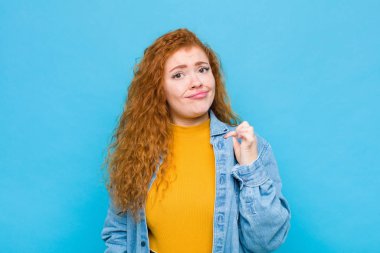 Genç kızıl saçlı kadın kibirli, başarılı, pozitif ve gururlu görünüyor. Mavi duvara karşı kendini işaret ediyor.