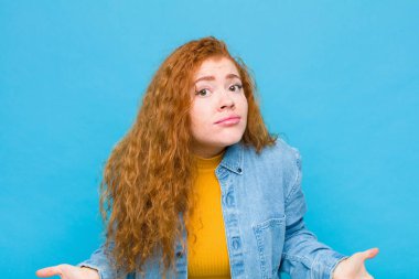 Genç kızıl saçlı kadın kendini budala ve kafası karışık hissediyor, hiçbir fikri yok, mavi duvara bakan aptal ya da aptal bir bakışla tamamen şaşkına dönmüş.