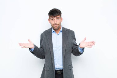 Genç yakışıklı adam şaşkın ve şaşkın, şüpheci, farklı seçenekleri tartıyor ya da beyaz duvara karşı komik bir ifadeyle seçiyor.