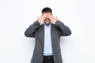 Genç yakışıklı adam gülümsüyor ve mutlu hissediyor, iki eliyle gözlerini kapatıyor ve beyaz duvara karşı inanılmaz bir sürpriz bekliyor.