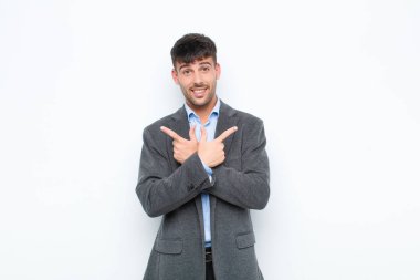 Genç yakışıklı adam şaşkın ve şaşkın görünüyor, güvensiz ve beyaz duvara karşı şüpheyle zıt yönleri işaret ediyor.