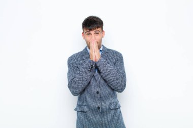 Genç yakışıklı adam mutlu ve heyecanlı, şaşırmış ve şaşırmış elleri ağızda, beyaz duvara karşı sevimli bir ifadeyle kıkırdıyor.