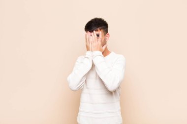 Genç yakışıklı adam elleriyle yüzünü kapatıyor. Şaşırmış bir ifadeyle parmaklarının arasından bakıyor ve sıcak duvara bakıyor.