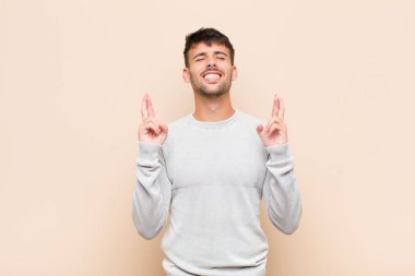 Genç yakışıklı adam gülümsüyor ve endişeyle iki parmağını çapraz yapıyor. Endişeli ve sıcak duvara karşı iyi şanslar diliyor ya da umut ediyor.