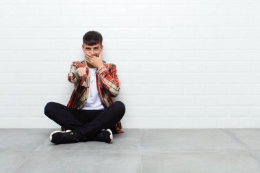 Genç yakışıklı adam sana gülüyor, kamerayı işaret ediyor ve seninle dalga geçiyor ya da çimento zeminde oturuyor.