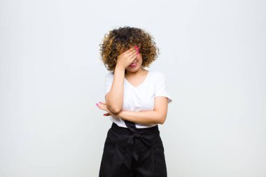 Genç, güzel bir kadın stresli, utanmış ya da üzgün görünüyor. Başı ağrıyor, yüzü beyaz duvara yaslanmış.