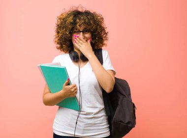 Genç ve güzel bir kız öğrenci. Mutlu, neşeli, şanslı ve şaşkın görünüyor. İki elini de pembe duvara dayayıp ağzını kapatmış.