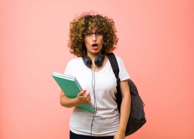 Genç ve güzel bir kız öğrenci. Şok olmuş ya da şaşırmış görünüyor. Ağzı açık pembe duvara karşı 