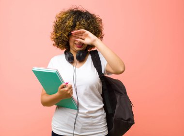 Genç, güzel, stresli, yorgun ve hayal kırıklığına uğramış görünen, alnından ter damlayan, pembe duvara karşı umutsuz ve bitkin hisseden bir bayan öğrenci.