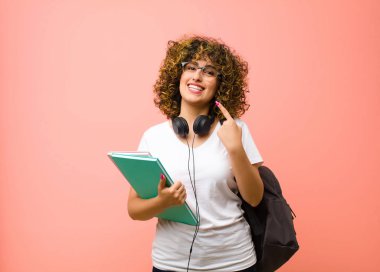 Genç ve güzel bayan öğrenci mutlu, arkadaş canlısı ve pozitif hissediyor, gülümsüyor ve elleri pembe duvara dayalı bir portre veya fotoğraf çerçevesi yapıyor