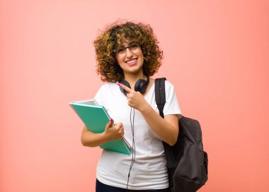 Genç ve güzel bayan öğrenci neşeyle gülümsüyor, mutlu hissediyor ve yan ve yukarı doğru işaret ediyor, fotokopi odasında pembe duvara karşı nesne gösteriyor.