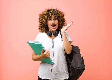 Genç ve güzel bir bayan öğrenci mutlu ve heyecanlı görünüyor. Beklenmedik bir sürprizle şoke oldu. İki eli de pembe duvara dayalı.