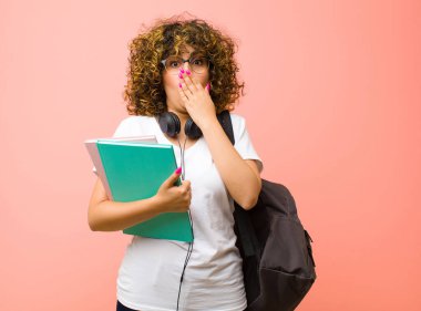 Genç, güzel bir bayan öğrenci endişeli, üzgün ve korkmuş hissediyor, elleriyle ağzını kapatıyor, endişeli görünüyor ve pembe duvara çarpmış gibi görünüyor.