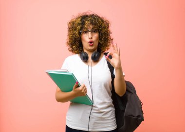 Genç, güzel bir bayan öğrenci şok olmuş, şaşırmış ve şaşırmış hissediyor. İki elini de pembe duvara yaslayarak onay veriyor.