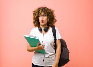 Genç ve güzel bir kadın kendini şaşkın, mutlu, şaşkın ve şaşırmış hissediyor. Ağzı açık pembe duvara bakıyor.