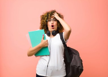 Genç ve güzel bayan öğrenci dehşete kapılmış ve şok olmuş hissediyor. Elleri havada ve pembe duvara karşı panikliyor.