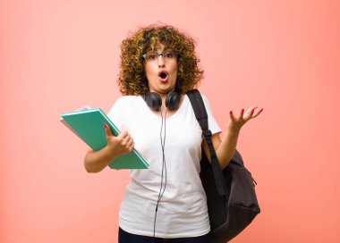 Genç ve güzel bir kız öğrenci, pembe duvara karşı aşırı derecede şok olmuş, şaşırmış, endişeli ve paniklemiş hissediyor.