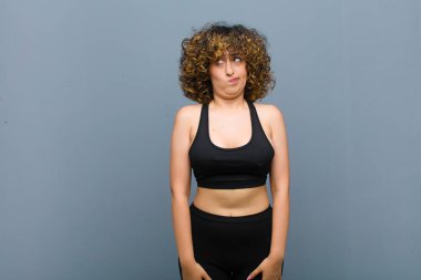 Genç sporcu kadın şaşkın ve şaşkın görünüyor, bir sorunu çözmeye çalışıyor ya da gri duvara karşı düşünüyor.