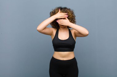 Genç sporcu kadın kameraya hayır diyen iki eliyle yüzünü kapatıyor! Resimleri reddetmek ya da gri duvara karşı fotoğraf yasaklamak