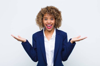 Afrikalı genç bir kadın mutlu, heyecanlı, şaşırmış ya da şok olmuş hissediyor, gülümsüyor ve düz duvara karşı inanılmaz bir şeye şaşırıyor.