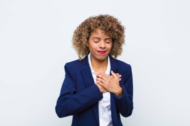 Afrikalı genç bir kadın üzgün, yaralı ve kalbi kırık görünüyor, iki elini de kalbe yakın tutuyor, ağlıyor ve yassı duvara karşı depresyona giriyor.