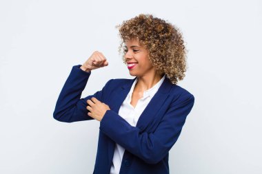 Genç Afro-Amerikan kadını mutlu, tatmin olmuş ve güçlü hissediyor, kaslı ve formda, spor salonundan sonra düz duvara karşı güçlü görünüyor.