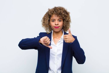 Afro-Amerikan genç kadın kafası karışmış, habersiz ve emin değil, iyi ve kötü seçenekleri ya da yassı duvara karşı tartıyor.